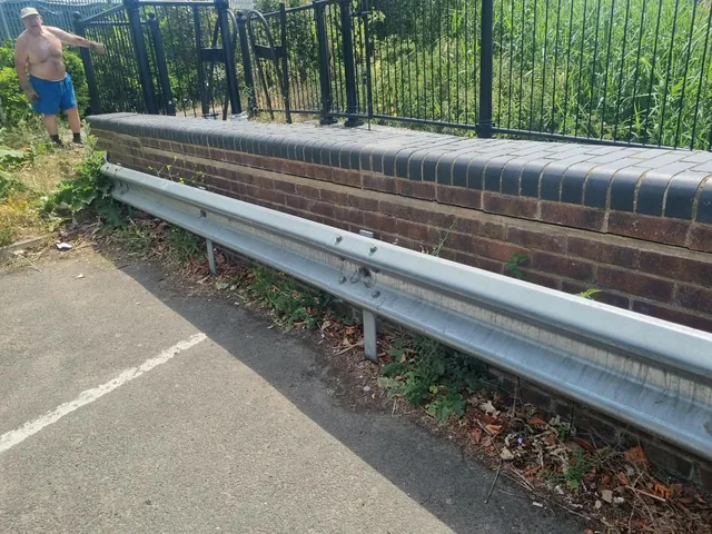 Steel roadside barrier below a brick boundary wall and railings