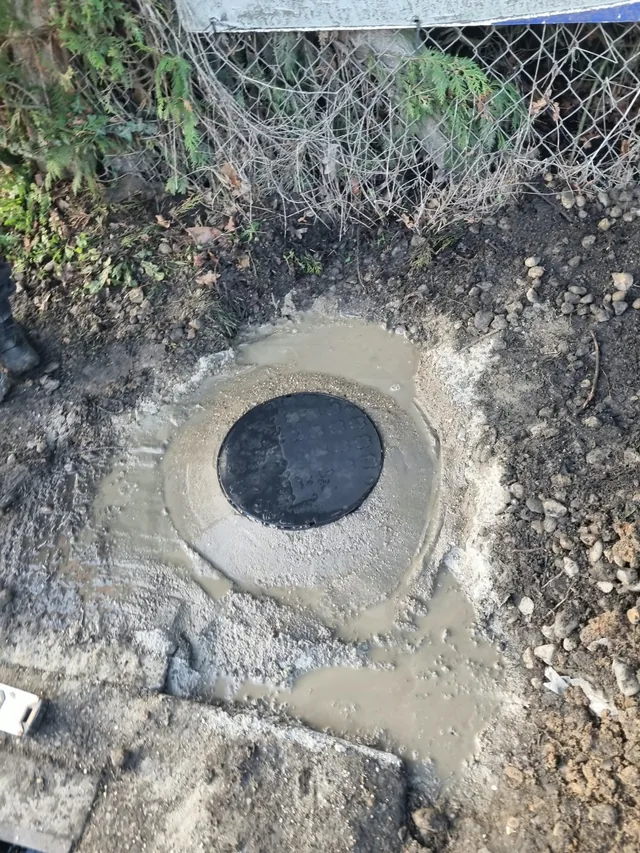 A circular drainage access cover set into a concrete surround