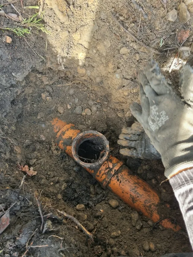 Excavated ground exposing an orange drainage pipe and its junction