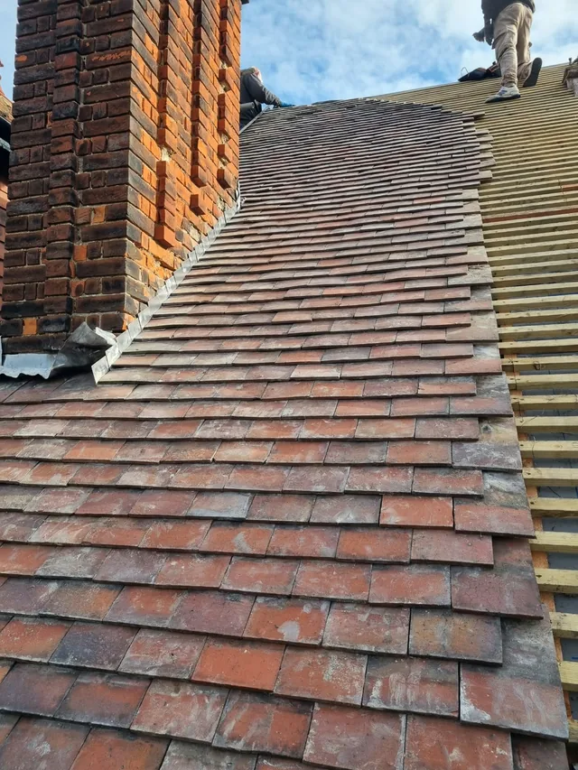Roof tiles being laid beside a brick chimney with battens still exposed