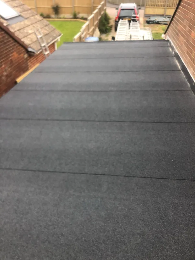 Flat roof covering with overlapping seams beside a brick wall