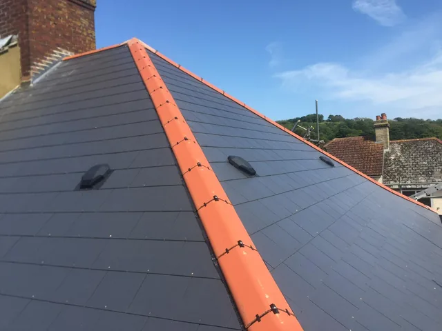 Dark roof tiles and red hip tiles beside a brick chimney