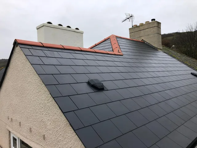 Dark tiled roof with red ridge tiles and rendered chimneys