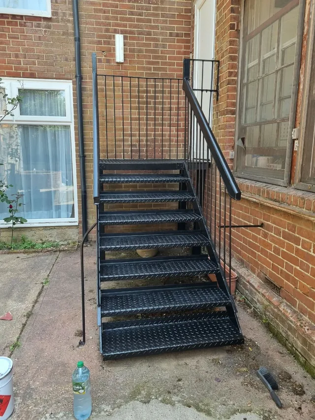 Short black-painted steel staircase beside a red-brick building