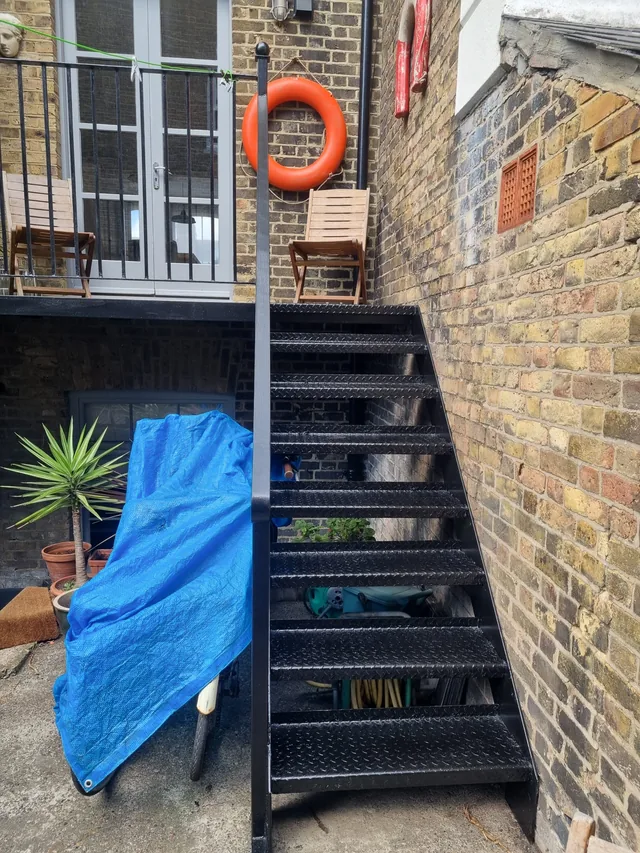 Short black steel staircase beside a lifebuoy and yellow-brick wall