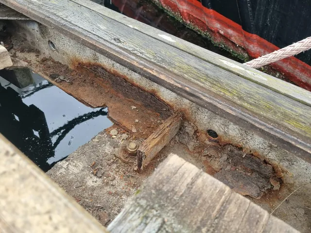 Corroded pontoon steelwork beneath timber boards above the water