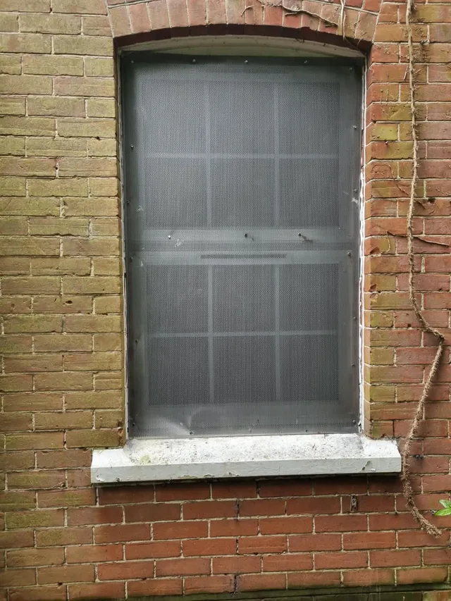Metal security panel covering a window opening in a brick building